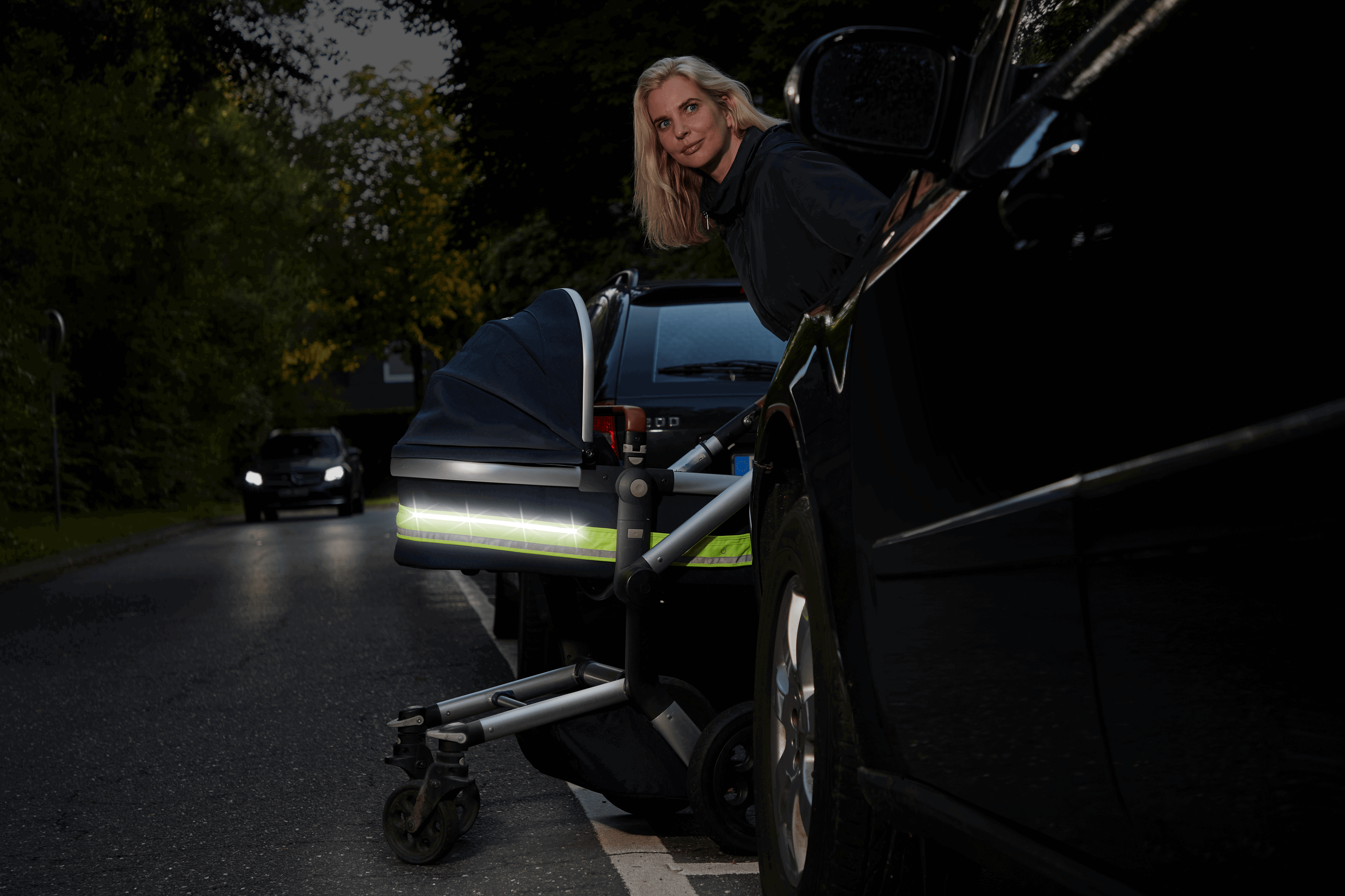 LED Kinderwagenlicht im Dunkeln – Seitenansicht, Frau schiebt Kinderwagen  mit leuchtenden LEDs im Straßenverkehr