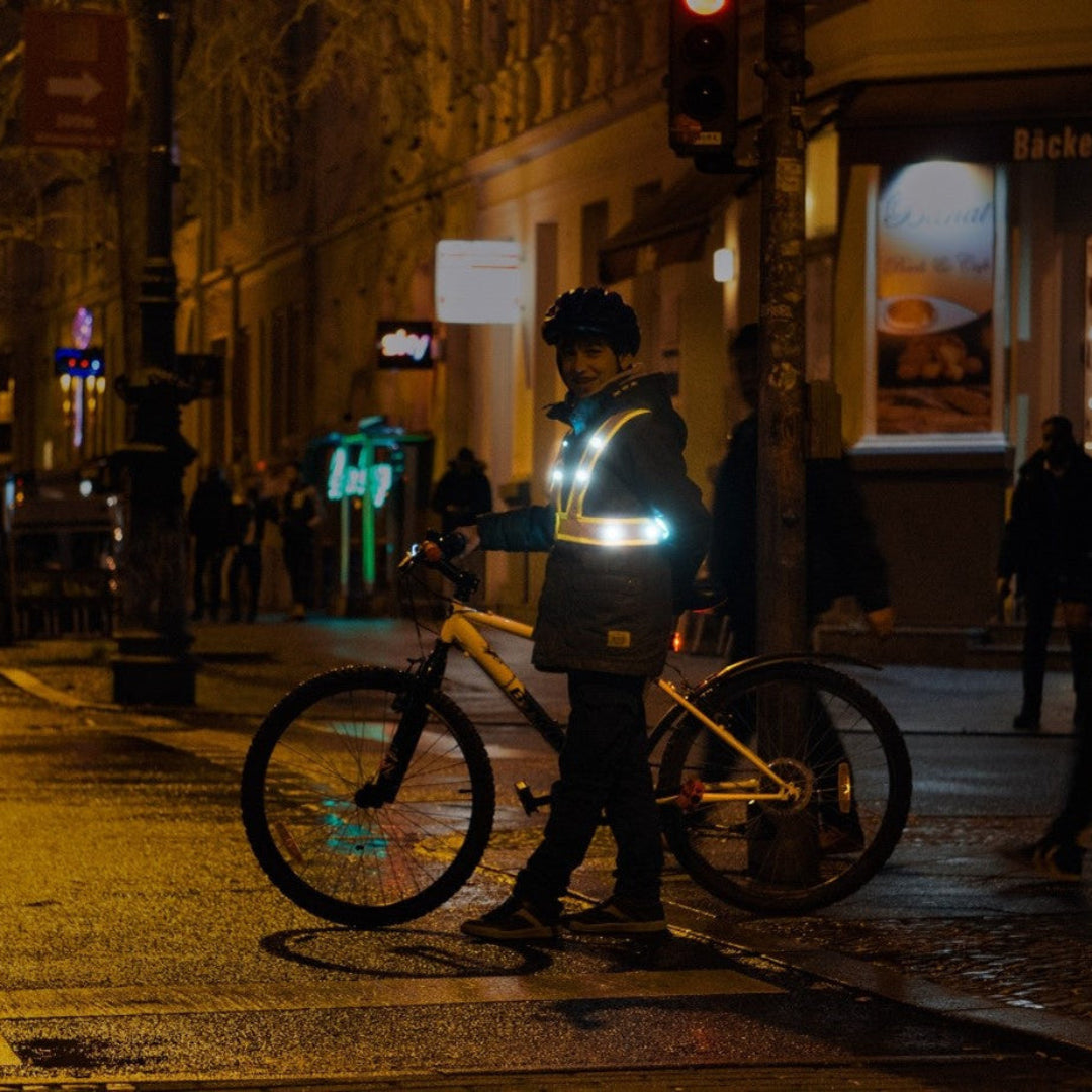 Kind mit LED Warnweste schiebt Fahrrad im Dunkeln – leuchtende LEDs im Straßenverkehr