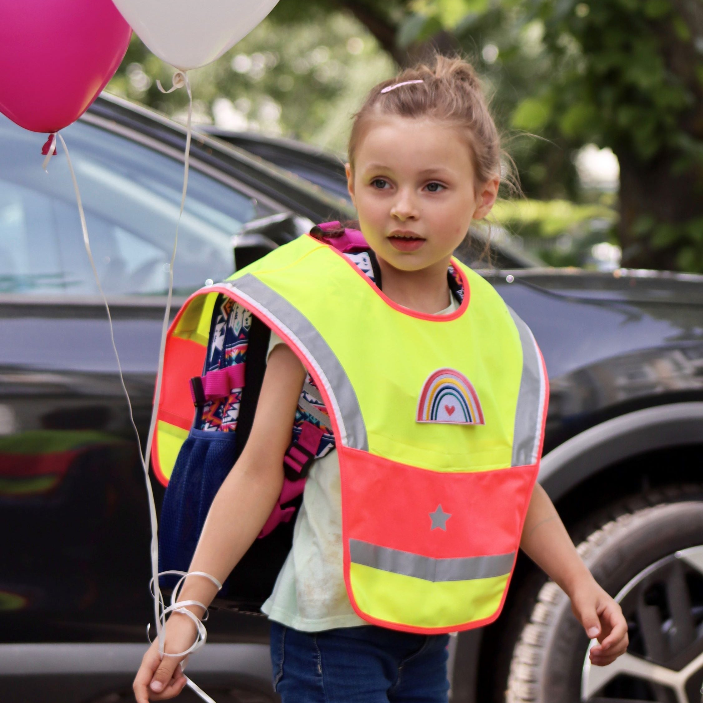 LED Warncape Kinder Regenbogen-Patch an Mädchen mit Luftballons, Auto im Hintergrund