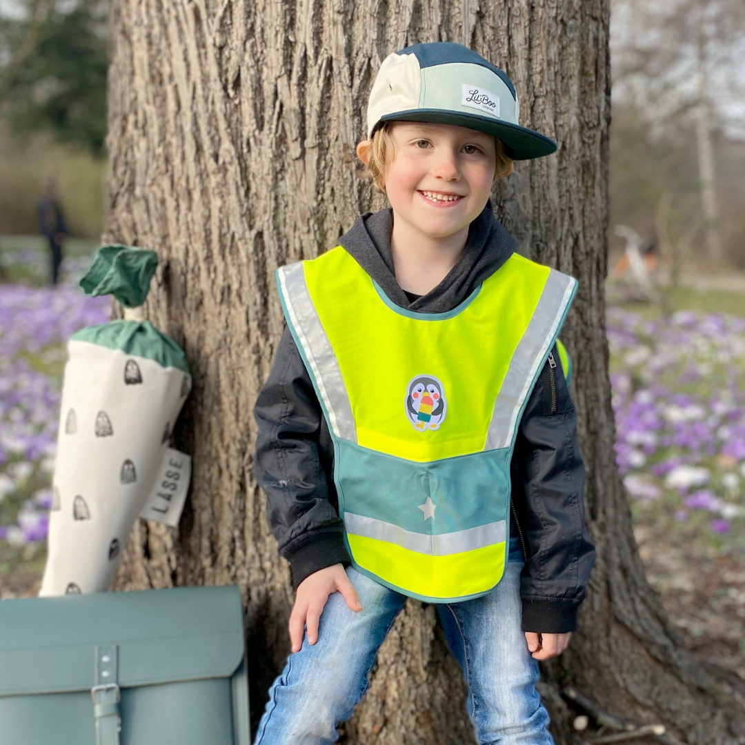 LED Warncape Kinder mit Pinguin-Patch an Junge mit Schultasche und Zuckertüte am Baum lehnend 